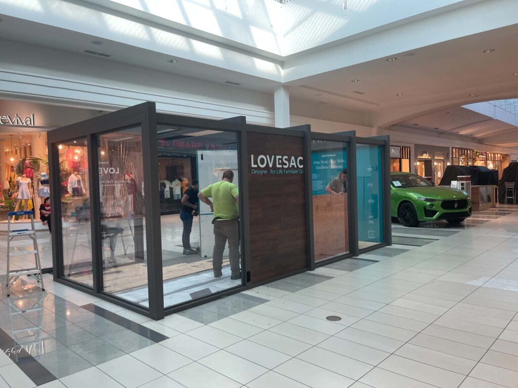 Crew members working inside a retail kiosk on the tiled floor of a shopping mall.