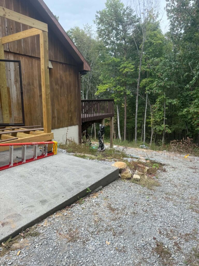 Area beside a wooden deck after the wood-debris pile was removed, with renovation work still visible.