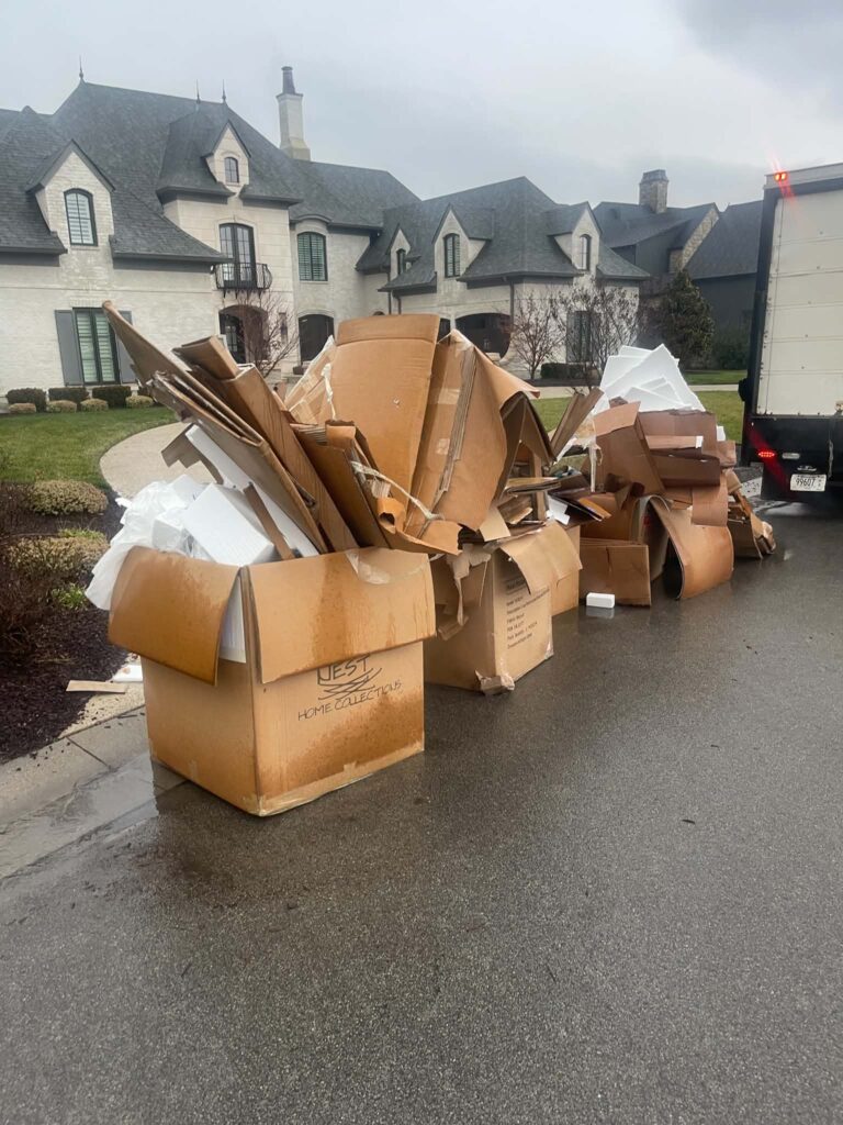 Cardboard boxes and packing foam piled beside a wet residential street before pickup