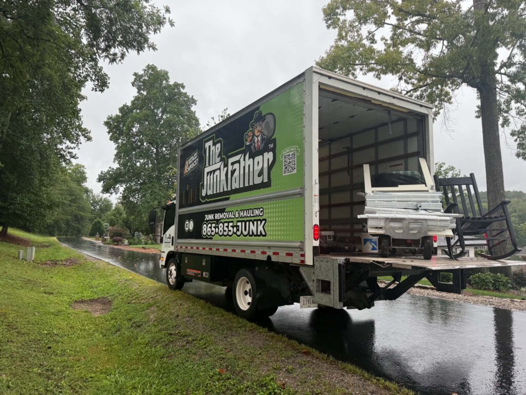 Items on the loading ramp of The JunkFather truck beside a wet road in Tellico Village.