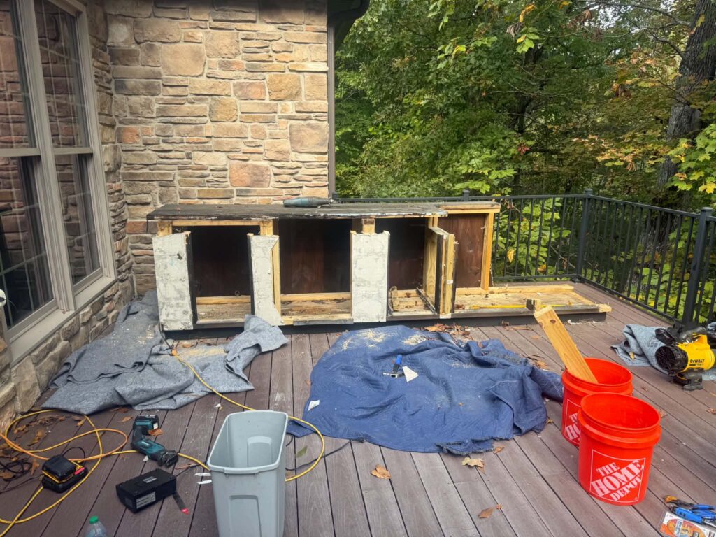 Built-in grill island partly dismantled with exposed wood framing and moving blankets protecting the deck