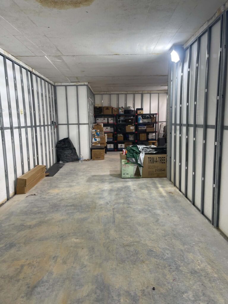 Boxes on shelving, a black bag and loose boards in the basement before sorting and debris removal.