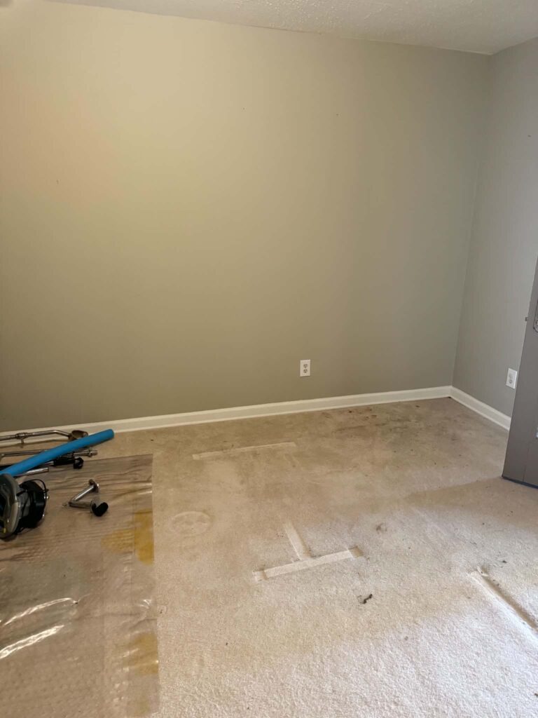 Room after the bulky gym equipment was removed, with carpet and a few small items remaining on the floor.