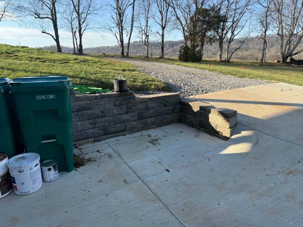 Concrete pickup area after the bulky items were hauled away, with bins and containers remaining beside the retaining wall.