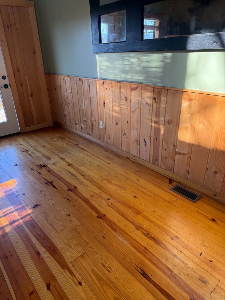 Cleared wood-floored cabin living room with green walls, wood trim and a wall mirror after the old furniture was removed