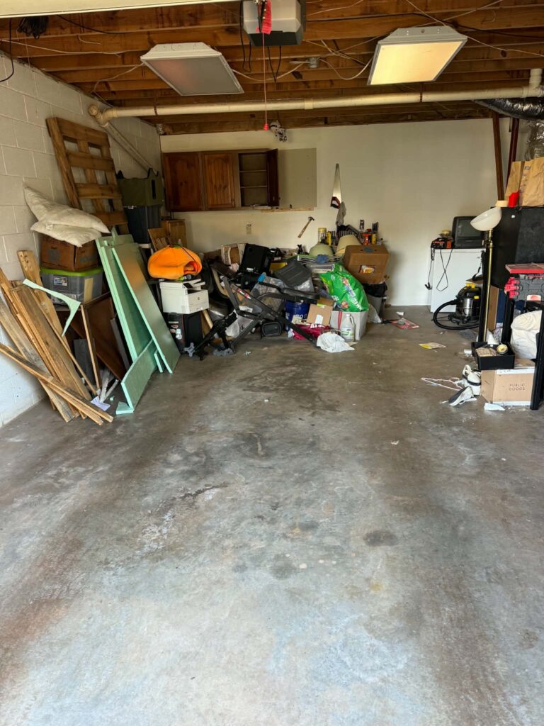 Central concrete floor visible after a garage furniture pickup, with stored items remaining at the sides and rear