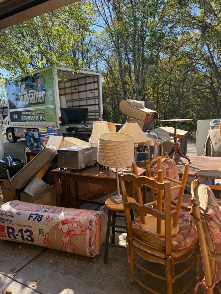 Estate pickup items including wooden chairs, tables, lamps and boxes beside The JunkFather truck