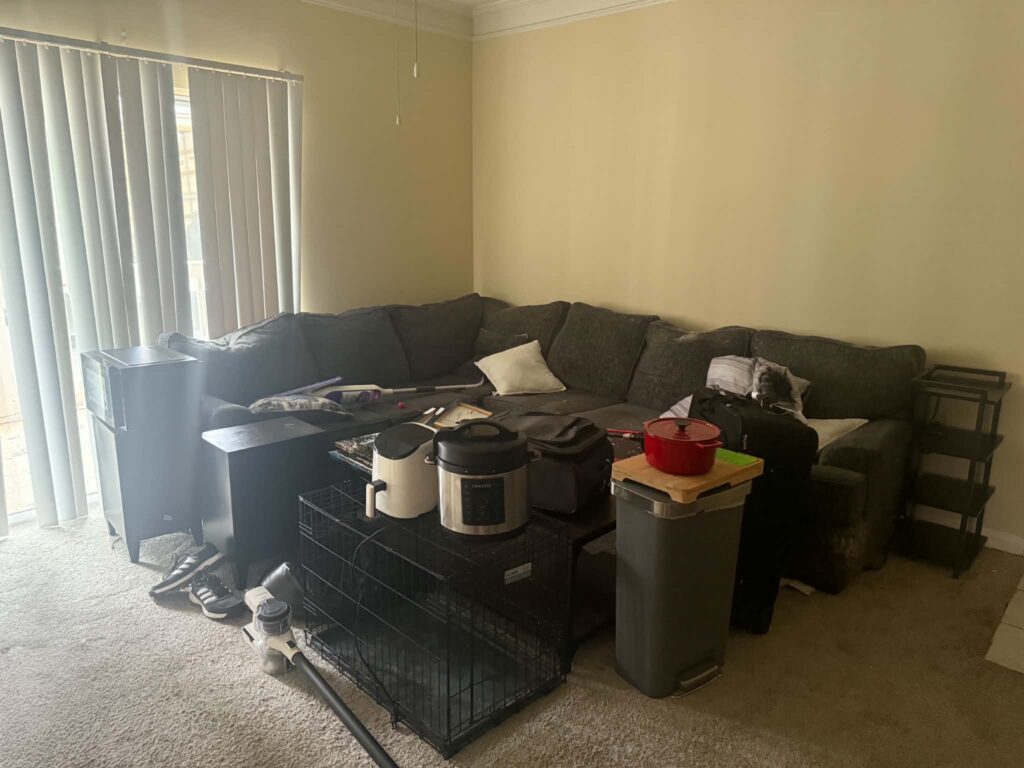 Sectional sofa, coffee table, shelving and remaining household items in a carpeted apartment living room before removal
