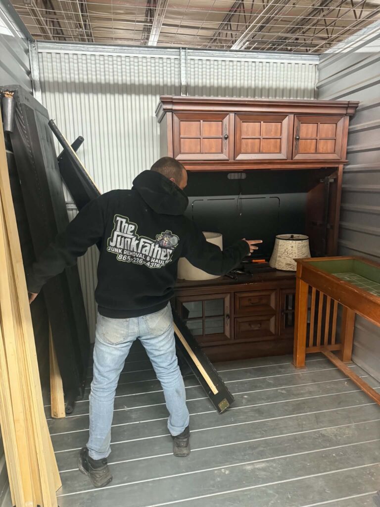 Worker inside a storage unit beside large wooden furniture during a cleanout.
