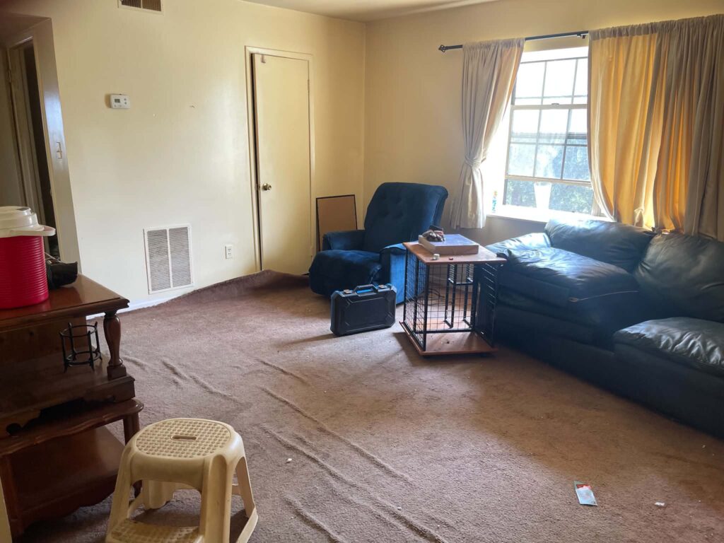 Furniture remaining in a rental living area while sections of carpet are being removed during an eviction cleanout