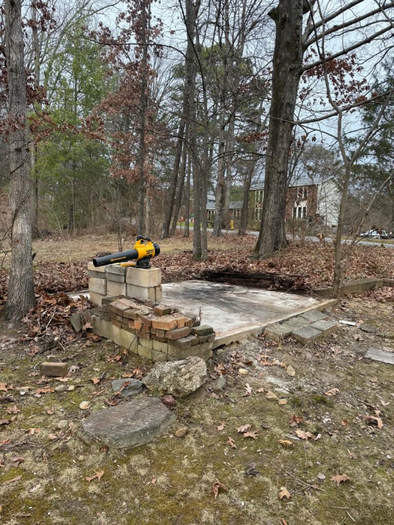 Exposed concrete pad and stacked masonry after the small backyard shed was removed.
