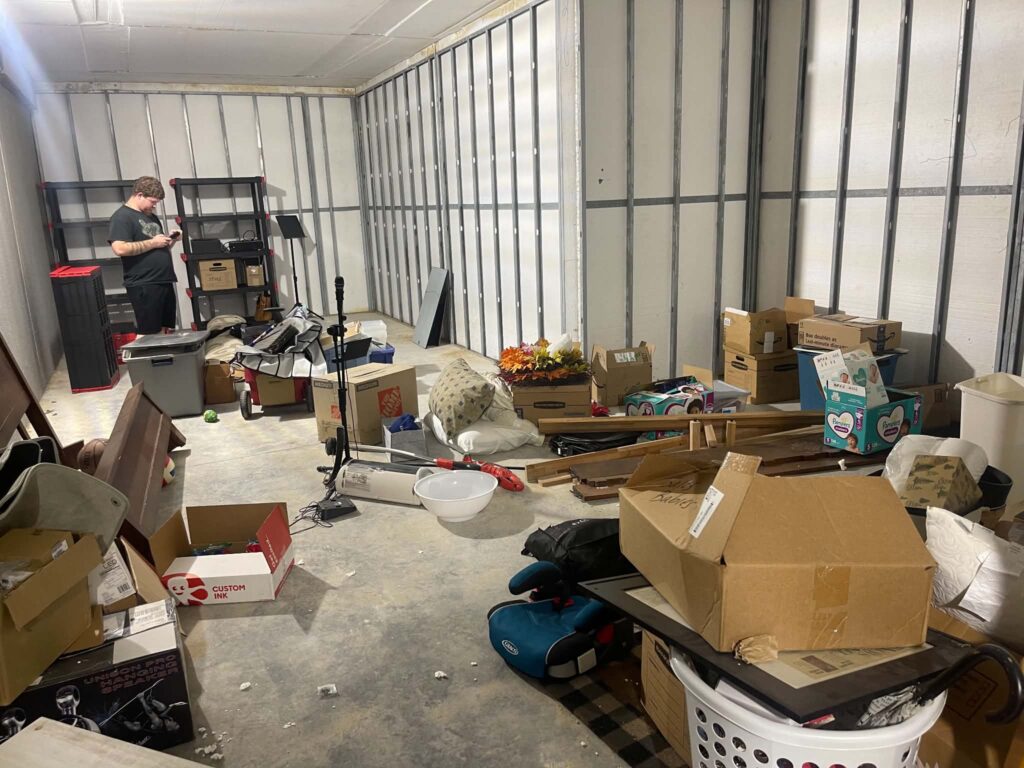 Wide view of the basement with boxes, storage bins and household belongings spread across the floor before the cleanout.