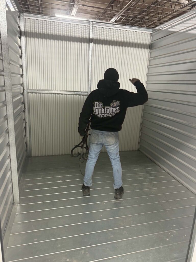 Crew member in a metal-walled storage unit after the bulky furniture has been removed.