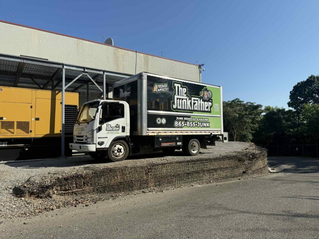 The JunkFather's branded white box truck parked beside a utility building and yellow generator.