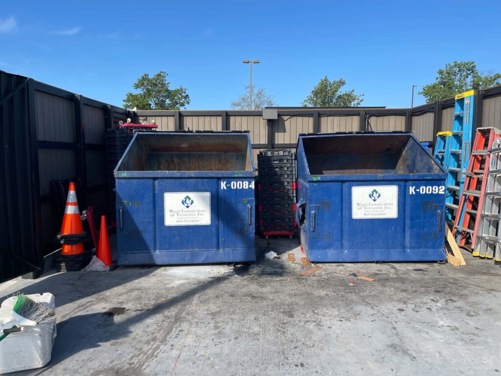 Blue commercial dumpsters remaining in the restaurant service area after excess material was removed.