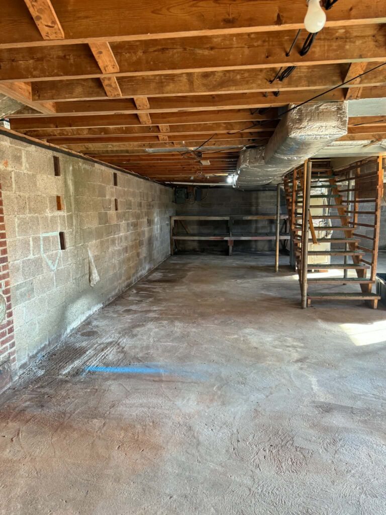 Additional view of the basement after removal, with open floor space, block walls and stairs remaining.