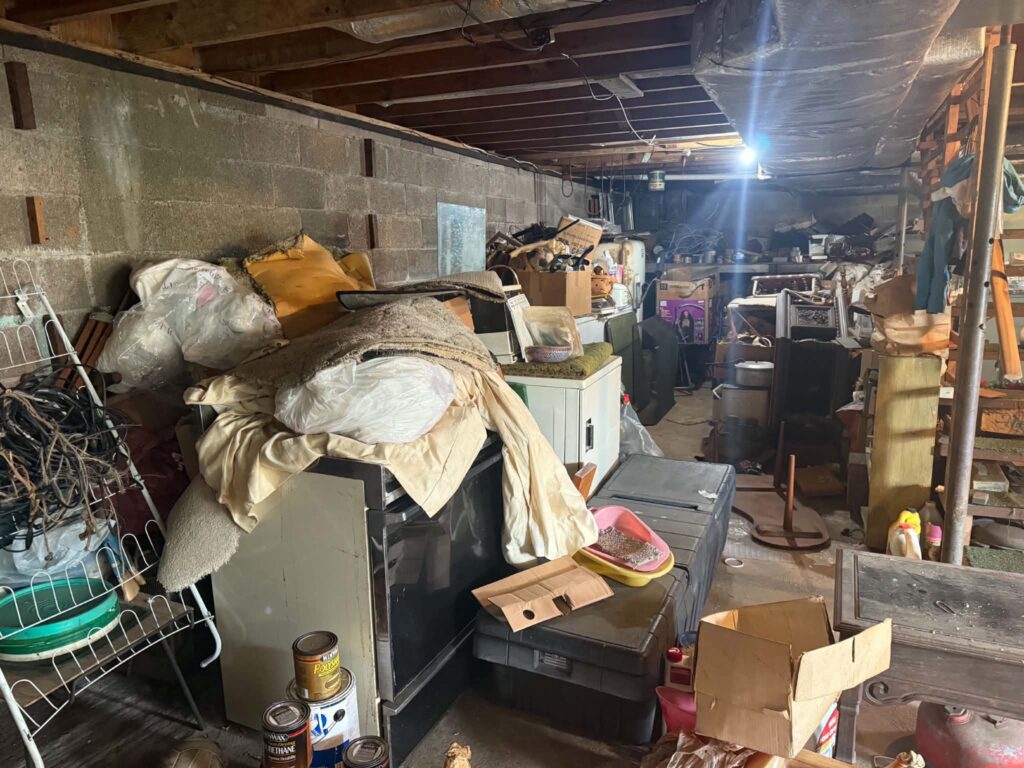 Furniture, bedding and boxes filling the basement beside a block wall.