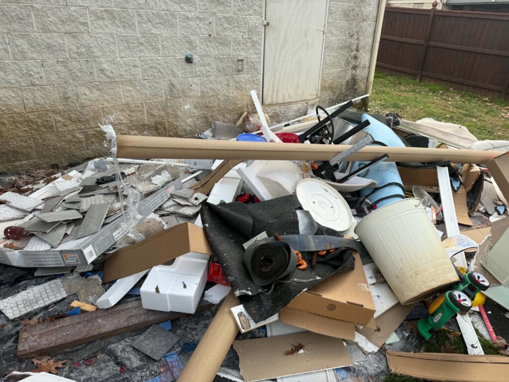 Flooring and mixed remodeling debris piled beside a house before hauling.