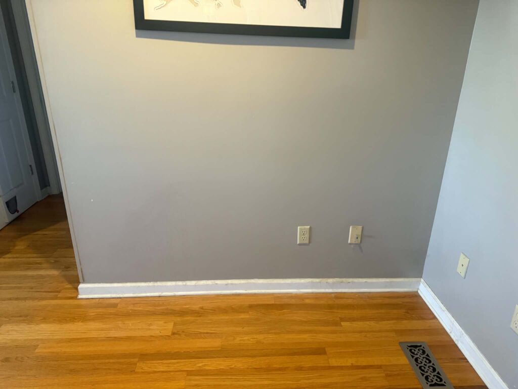 Open floor space against the same gray wall after the upright piano was removed.