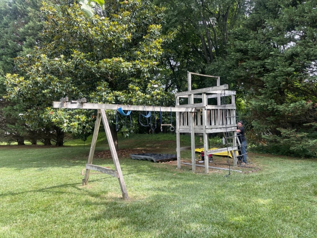 Crew member dismantling a weathered wooden playset with swings in a Farragut backyard.