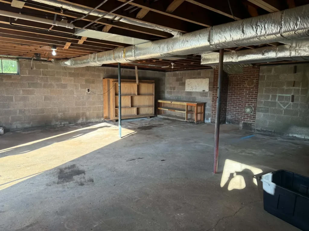 Basement after removal, with open floor space, shelving and a workbench remaining.