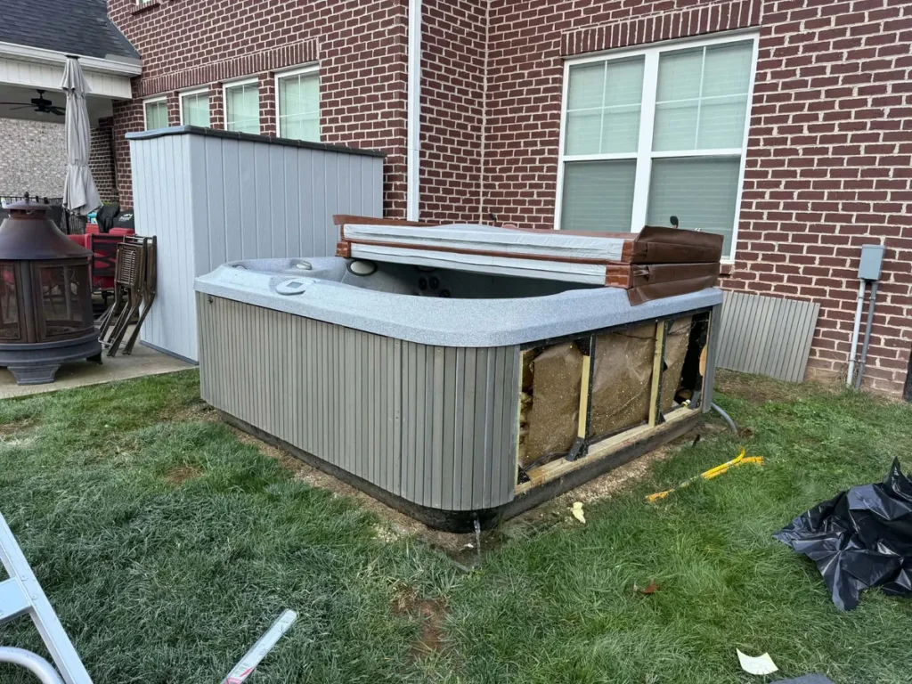 Gray outdoor hot tub beside a brick house before removal