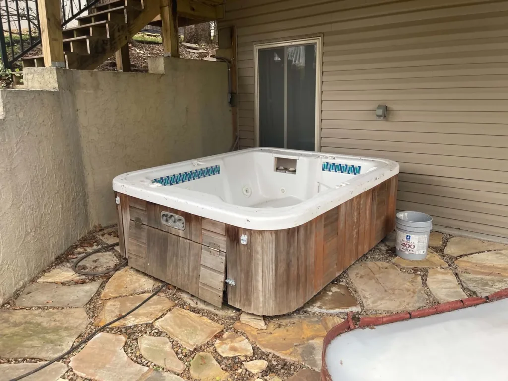 Wood-sided hot tub on a stone patio beneath an elevated deck before removal