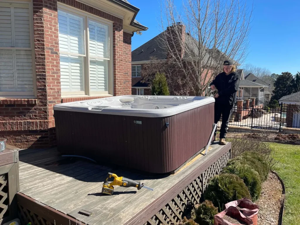 Brown hot tub on a raised wooden deck beside a brick home before removal