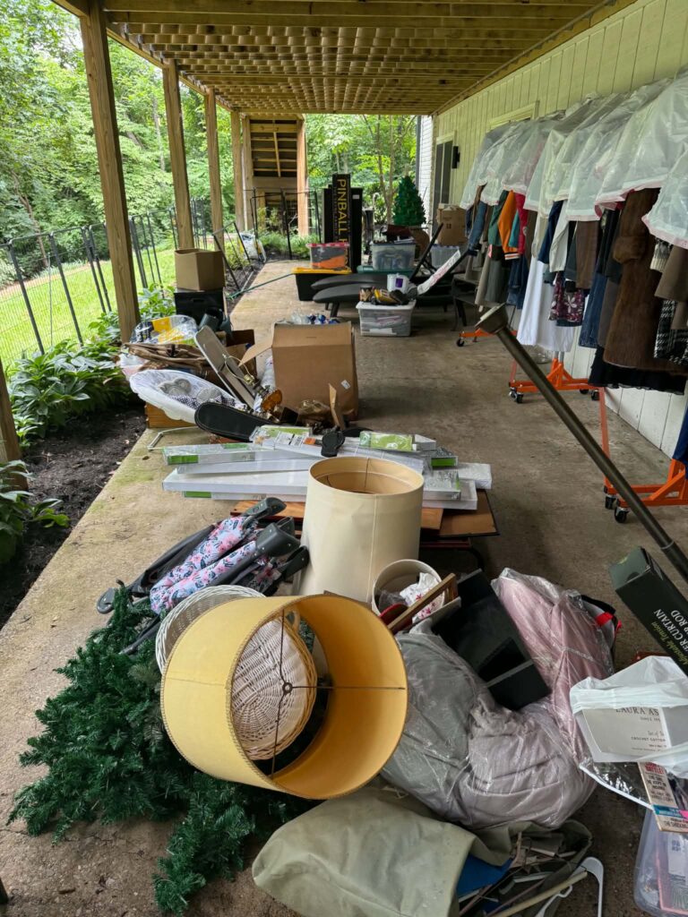 Household items, storage containers, and lamps under a raised deck before junk pickup.
